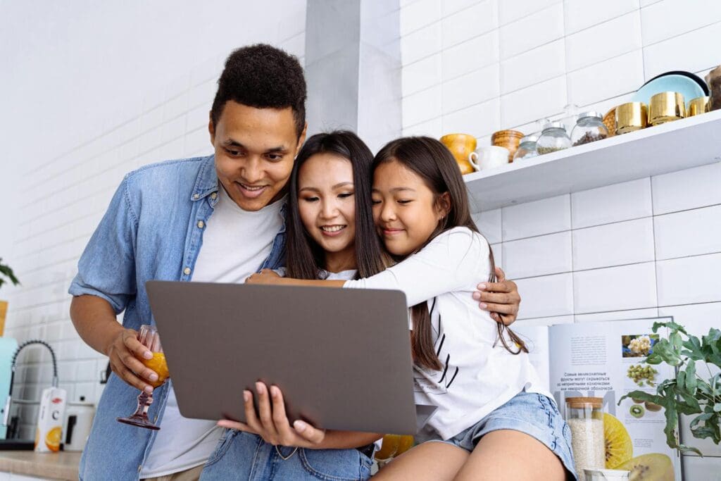 A joyful family of three browsing content together on a laptop at home.