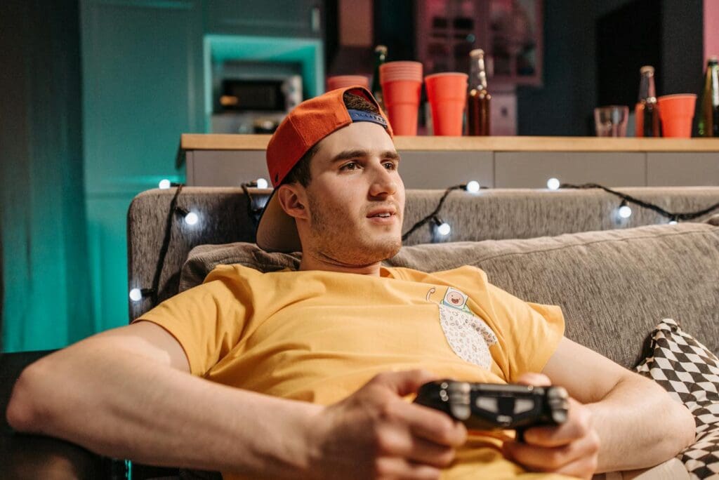 Adult man wearing a yellow shirt and cap, intensely gaming on a couch with a controller.