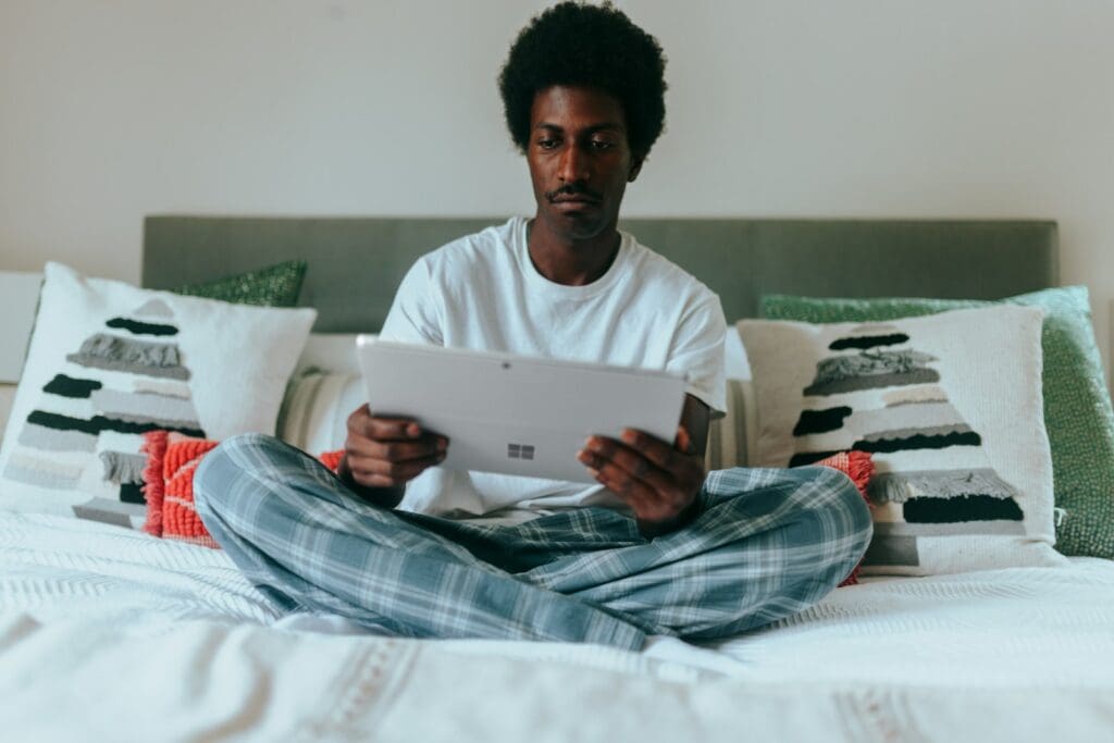 Man on his bed on his Surface laptop with holiday pillows behind