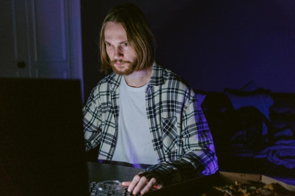 A young man intensely focused on gaming alone in a dimly lit room.
