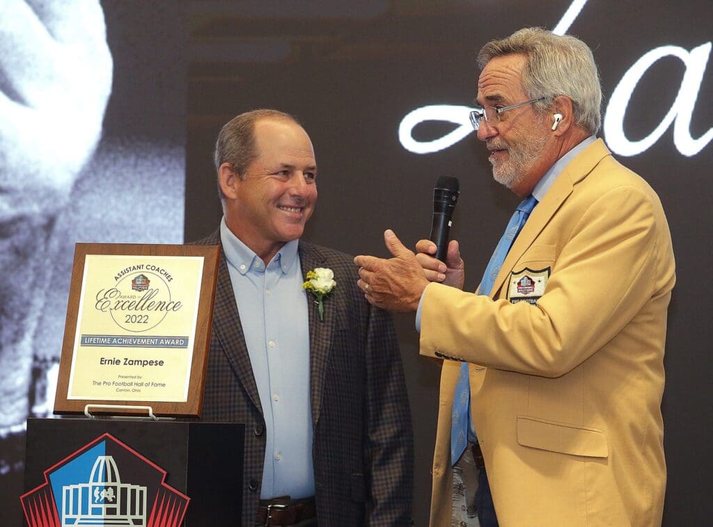 Ken Zampese ,left, accepts the Pro Football Hall of Fame Assistant Coaches Award of Excellence for his father Ernie Zampese from master of ceremonies Hall of Famer Dan Fouts at the Pro Football Hall of Fame Thursday, June 30, 2022. Ssh36241