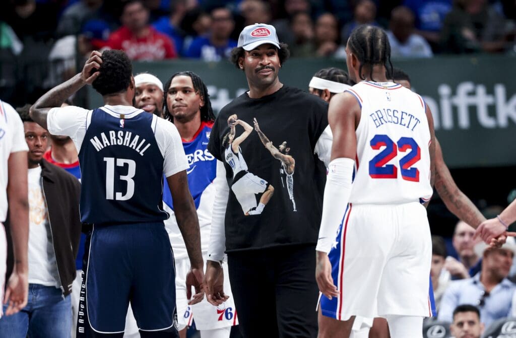 Mar 16, 2025; Dallas, Texas, USA; Philadelphia 76ers center Andre Drummond wears a shirt with Dirk Nowitzki and Tim Duncan during the second half in front of Dallas Mavericks forward Naji Marshall (13) and Philadelphia 76ers forward Oshae Brissett (22) at American Airlines Center. Mandatory Credit: Kevin Jairaj-Imagn Images