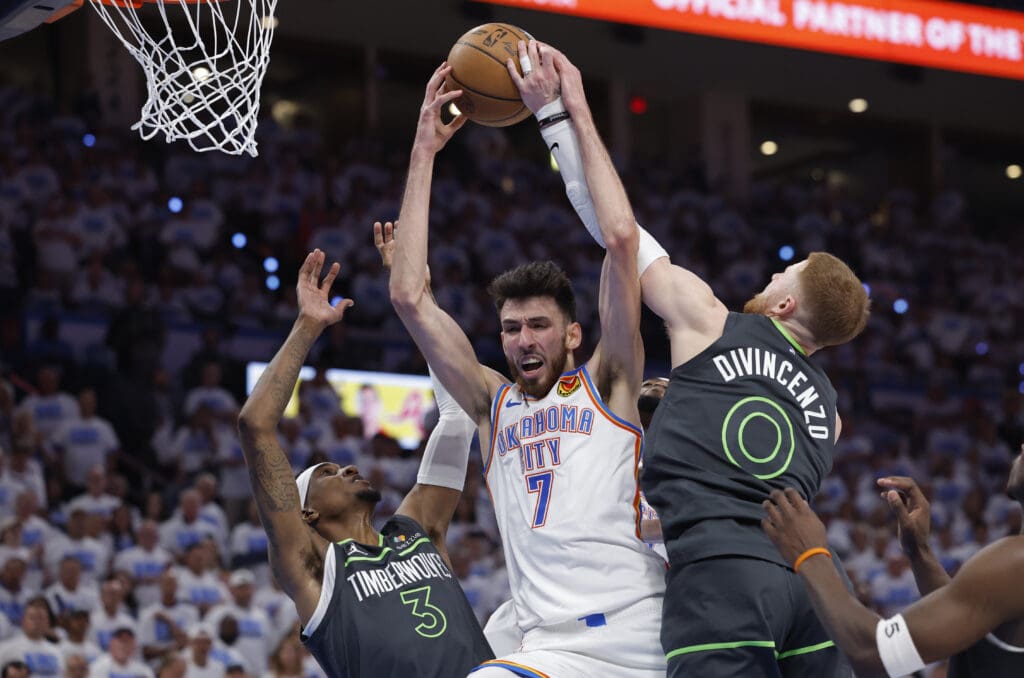 May 20, 2025; Oklahoma City, Oklahoma, USA; Oklahoma City Thunder forward Chet Holmgren (7) rebounds against Minnesota Timberwolves guard Donte DiVincenzo (0) and forward Jaden McDaniels (3) in the fourth quarter during game one of the western conference finals for the 2025 NBA Playoffs at Paycom Center.