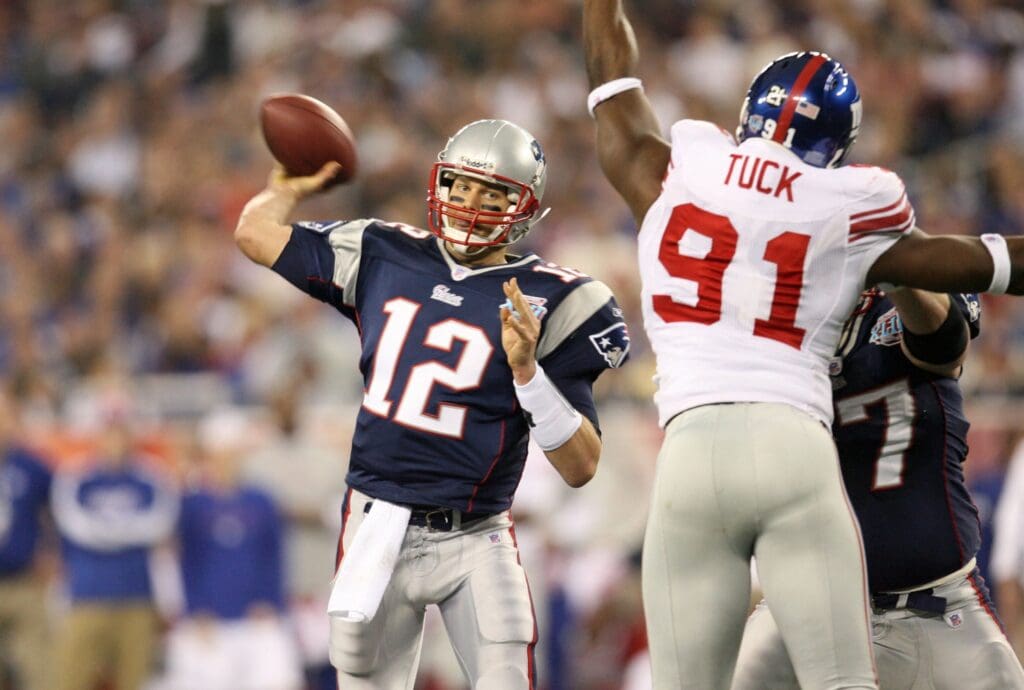 Feb 3, 2008; Glendale, AZ, USA; New England Patriots quarterback Tom Brady (12) passes past New York Giants defensive end Justin Tuck (91) in the first half of Super Bowl XLII at the University of Phoenix Stadium.